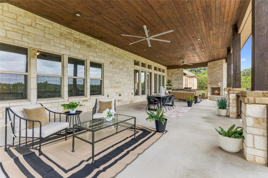 An inviting outdoor living area features a stone fireplace, wood-plank ceiling, and ample space for relaxation and dining.