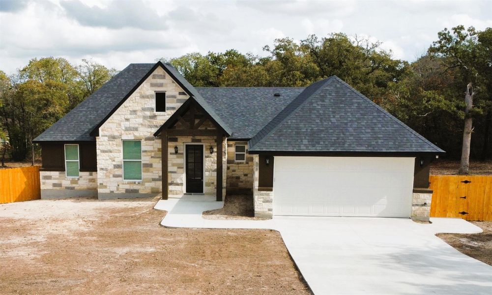 View of front of home with stone siding, driveway, an attached garage, and roof with shingles