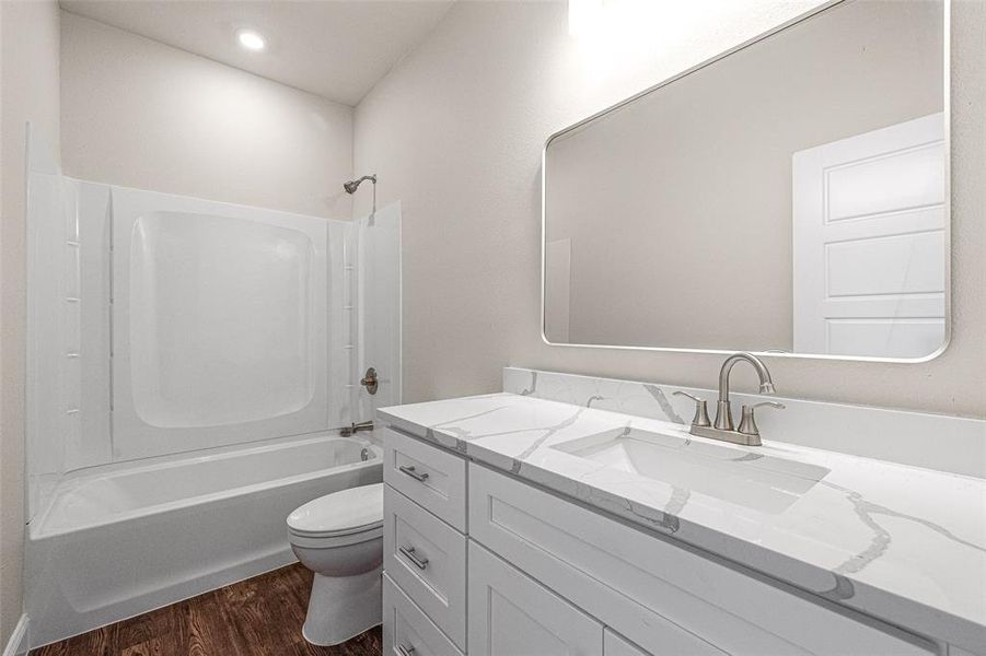 Full bathroom with washtub / shower combination, hardwood / wood-style flooring, toilet, and vanity with extensive cabinet space