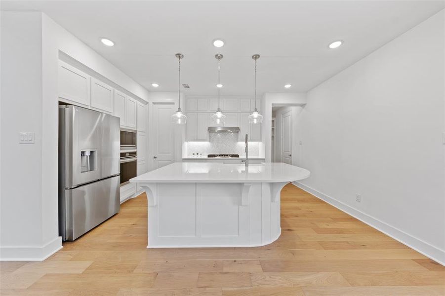 Kitchen featuring white cabinetry, light countertops, decorative backsplash, light wood finished floors, and appliances with stainless steel finishes