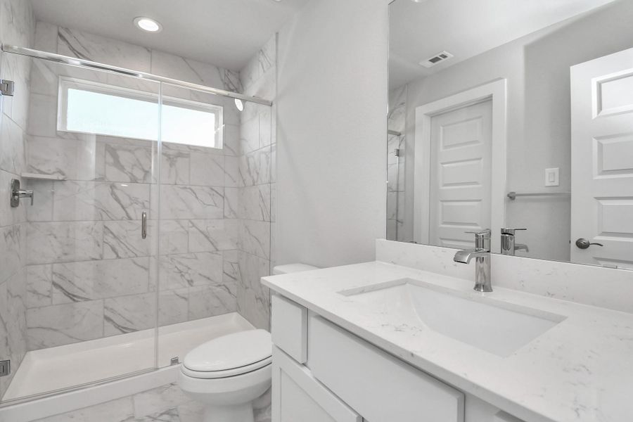 Secondary bath features tile walk-in shower with tile surround, light stained wood cabinets, beautiful light countertop. Sample photo of completed home with similar floor plan. Actual colors and selections may vary.