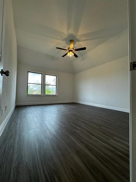 Empty room featuring vaulted ceiling, ceiling fan, and dark wood-type flooring