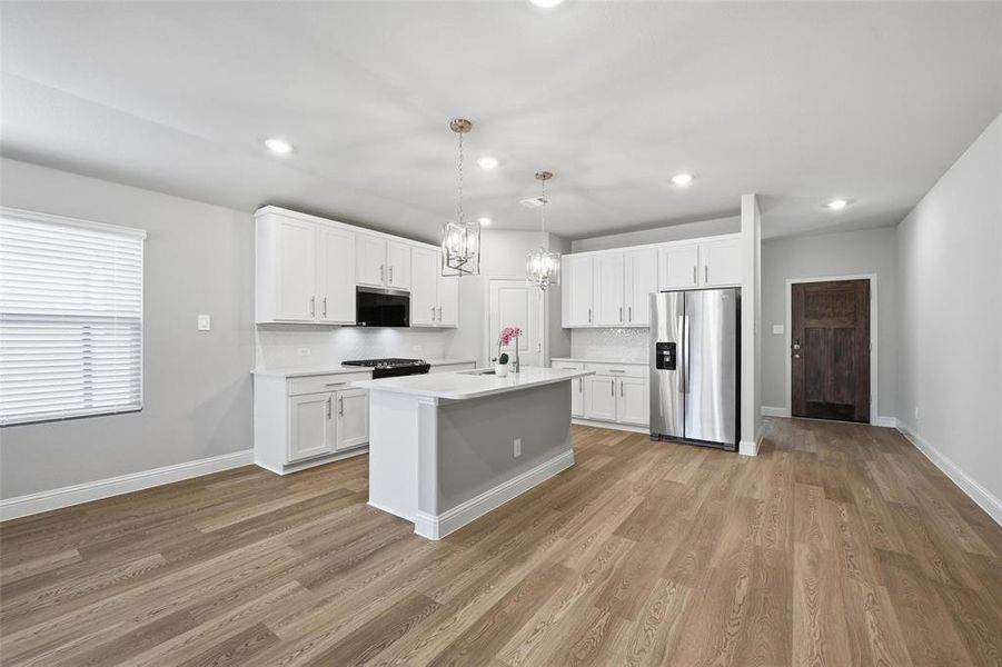 Kitchen featuring stainless steel appliances, white cabinetry, decorative light fixtures, a kitchen island with sink, and a chandelier