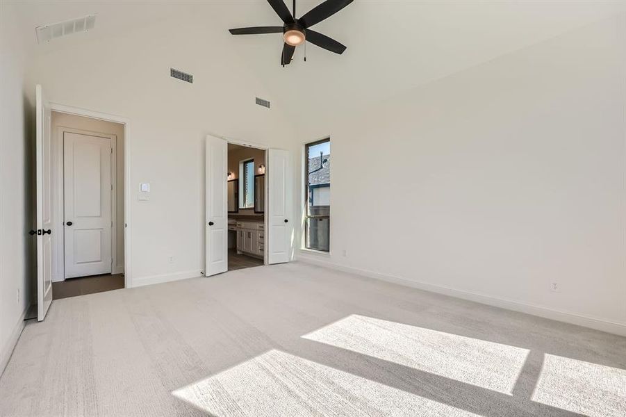 Main bedroom featuring ceiling fan, connected bathroom, light carpet, and high vaulted ceiling