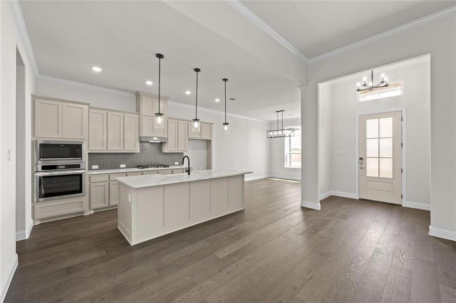 Kitchen featuring an island with sink, hanging light fixtures, tasteful backsplash, dark wood-type flooring, and appliances with stainless steel finishes