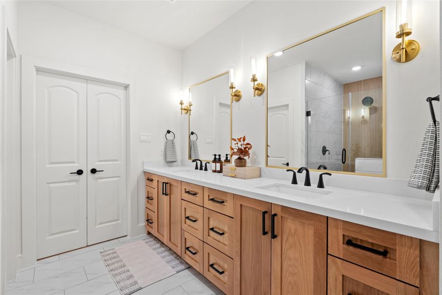 Luxurious primary bathroom featuring a double vanity with quartz countertops, modern matte black fixtures, and elegant gold-accented mirrors - combining warmth and sophistication in one space. Luxurious primary bathroom featuring a double vanity with quartz countertops, modern matte black fixtures, and elegant gold-accented mirrors - combining warmth and sophistication in one space.