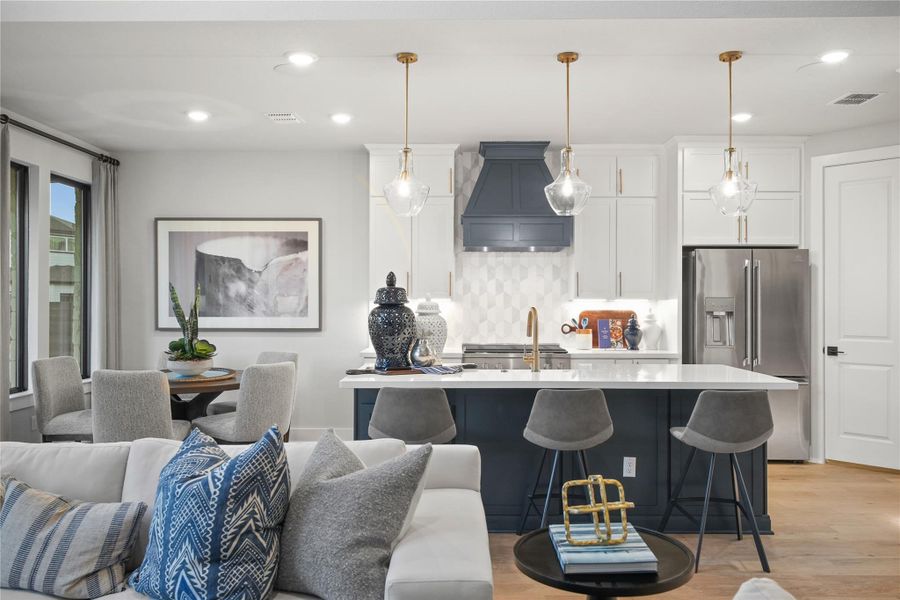 Kitchen featuring white cabinets, stainless steel refrigerator with ice dispenser, decorative backsplash, a breakfast bar area, and hanging light fixtures