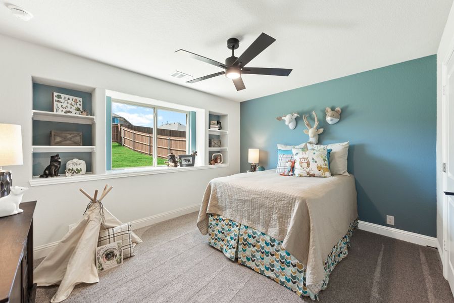 Children's bedroom with teal accent wall, built-in shelves, ceiling fan, and carpet flooring