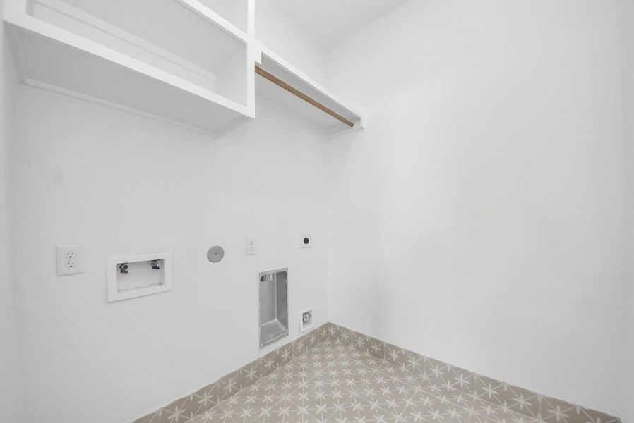 This bright laundry room combines style and function, with washer and dryer hookups, open shelving, and patterned tile flooring, making daily chores organized and efficient.