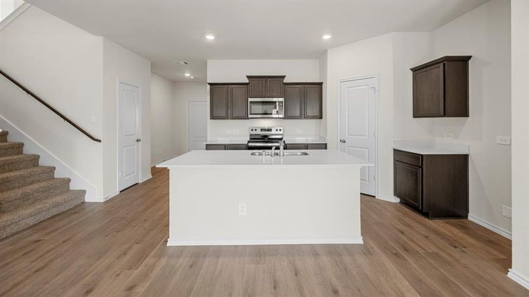 Kitchen with dark wood finish cabinets, a center island with sink, stainless steel appliances, light wood-type flooring, and recessed lighting