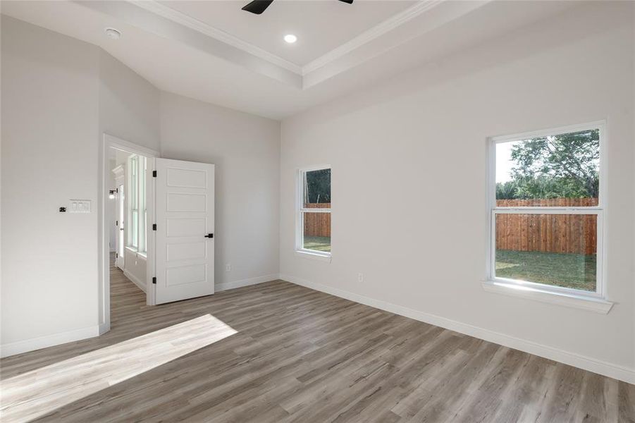 Main bedroom room featuring light wood finished floors, recessed lighting, crown molding, a tray ceiling, and ceiling fan.