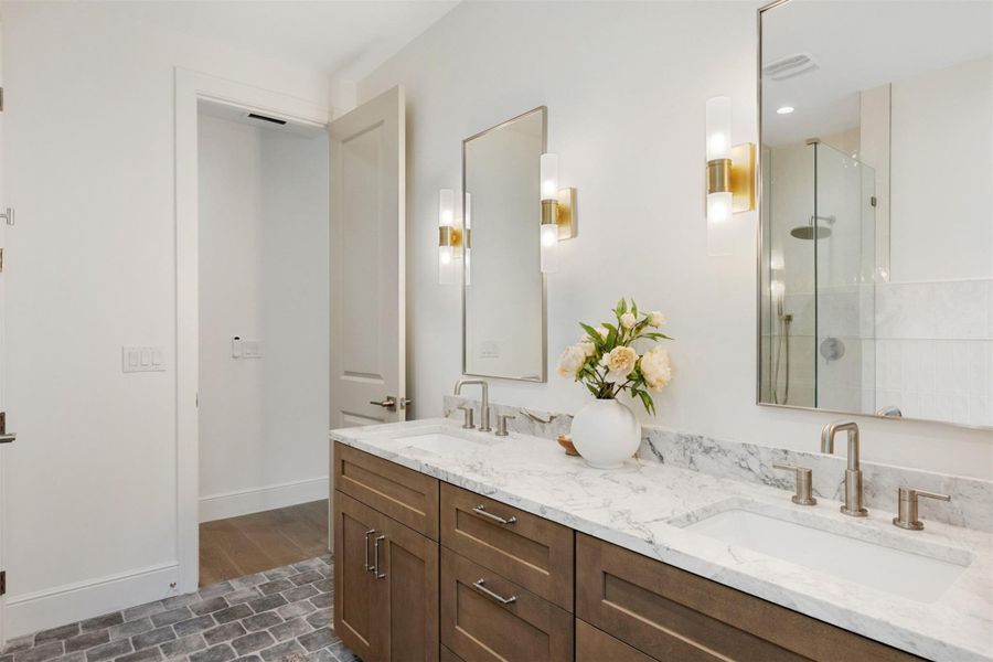 A well-lit bathroom features a double vanity with white marble countertops and stylish gold-accented sconces.