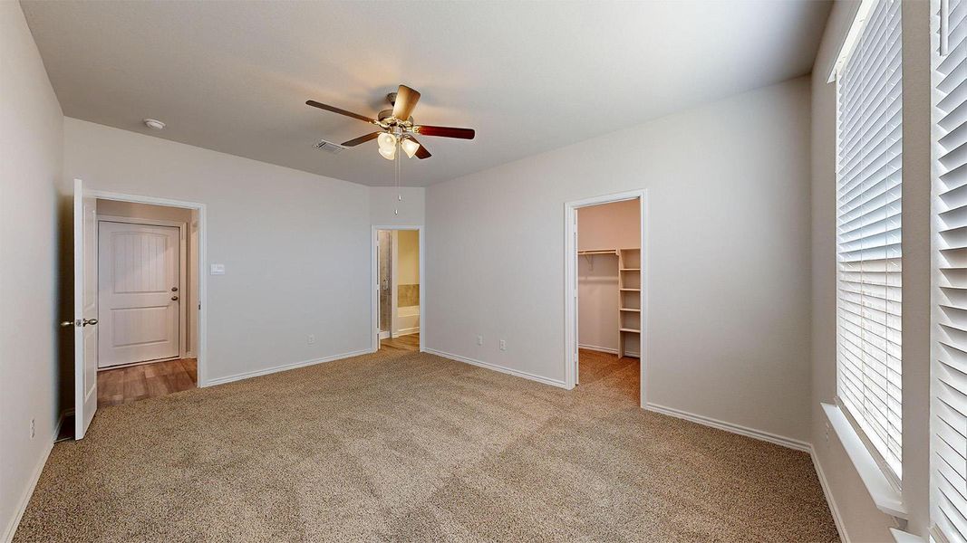 Unfurnished bedroom featuring light carpet, a spacious closet, and a ceiling fan
