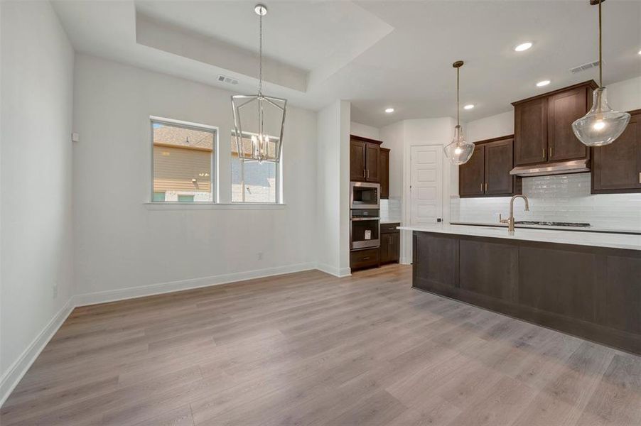 Open-concept kitchen and dining area featuring wood-finish flooring, recessed lighting, and a tray ceiling