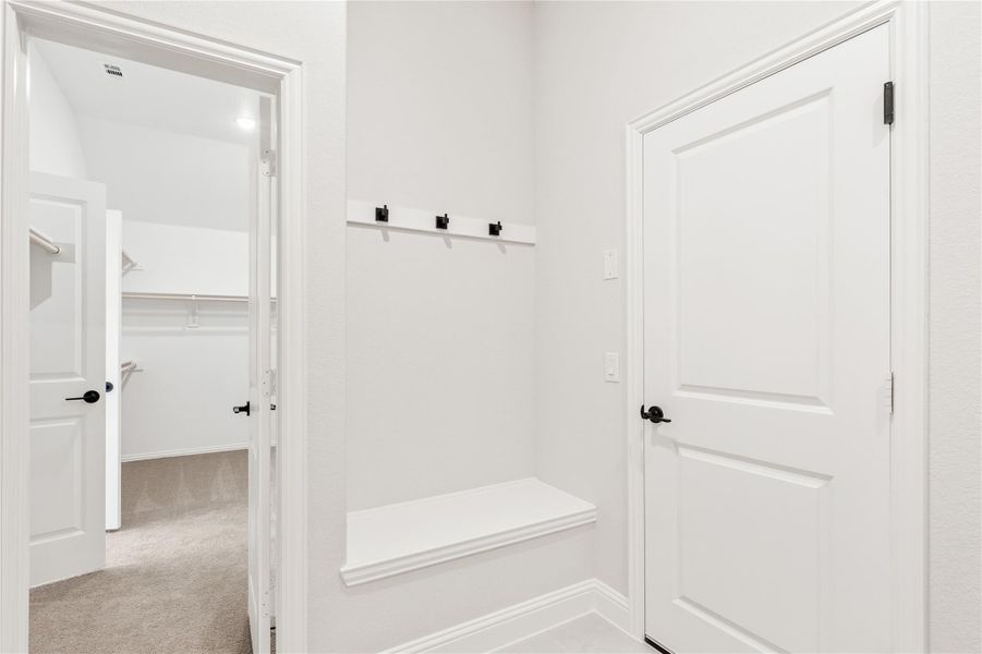 Mudroom area with built-in bench, wall hooks, and doorway leading to walk-in closet Mudroom area with built-in bench, wall hooks, and doorway leading to walk-in closet