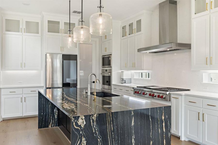 Kitchen with wall chimney exhaust hood, light wood-style flooring, stainless steel appliances, an island with sink, and white cabinets