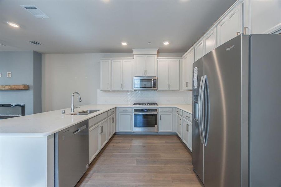 Kitchen featuring quartz peninsula contertops, appliances with stainless steel finish, hardwood flooring and white cabinets with door handles - View