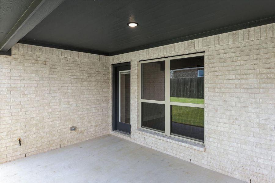 Covered back patio with light brick walls, dark ceiling, recessed light, and sliding glass door to backyard Covered back patio with light brick walls, dark ceiling, recessed light, and sliding glass door to backyard