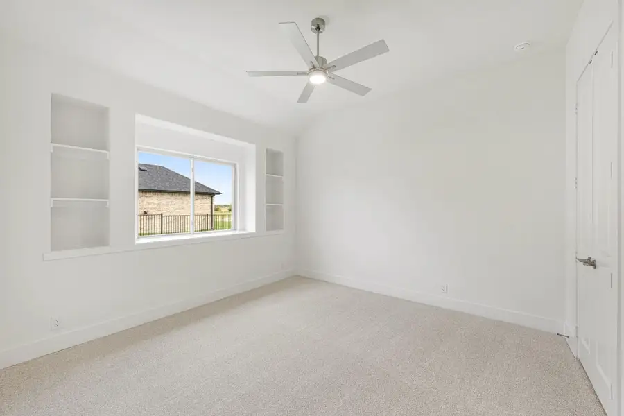 Empty bedroom with vaulted ceiling, ceiling fan, built-in shelves, and carpet flooring Empty bedroom with vaulted ceiling, ceiling fan, built-in shelves, and carpet flooring