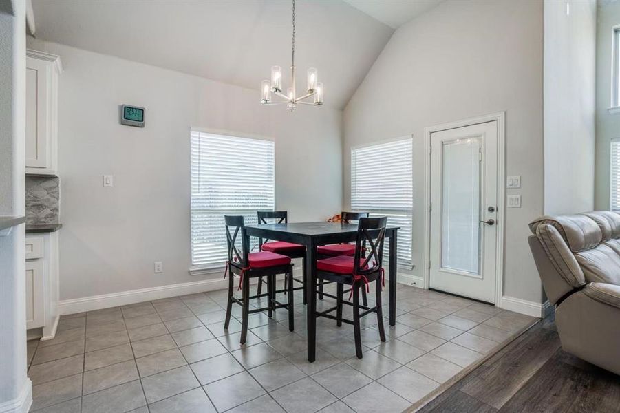 Dining area with a chandelier, light tile patterned flooring, and high vaulted ceiling