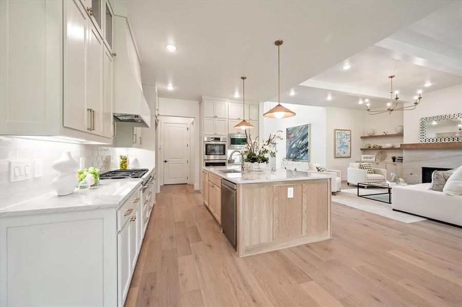 Kitchen with white cabinetry, light stone countertops, light wood-type flooring, and an island with sink