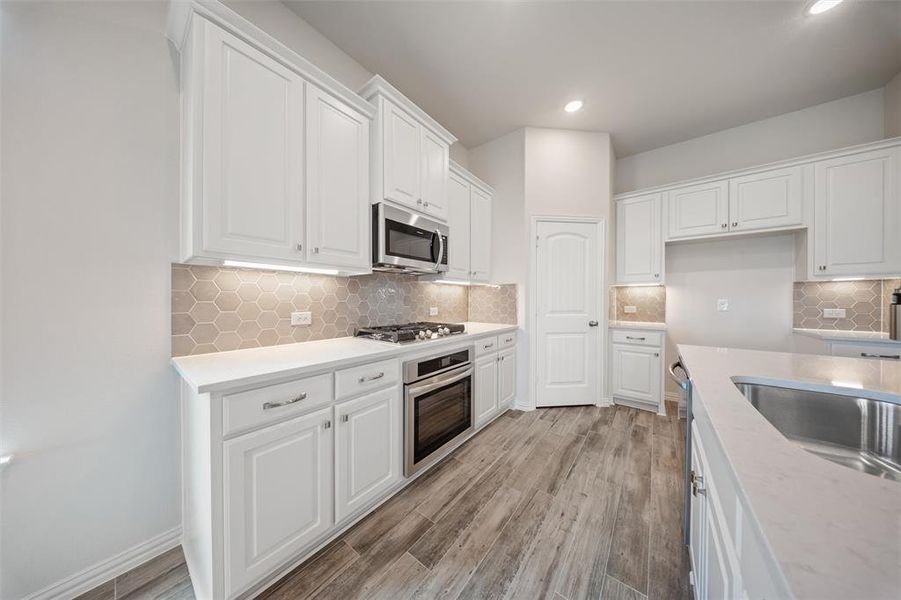 Kitchen with white cabinetry, light wood-style flooring, stainless steel appliances, light countertops, and recessed lighting