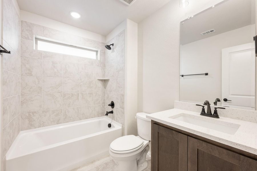 Bathroom with tiled tub-shower combo, dark wood vanity, white quartz countertop, and black fixtures