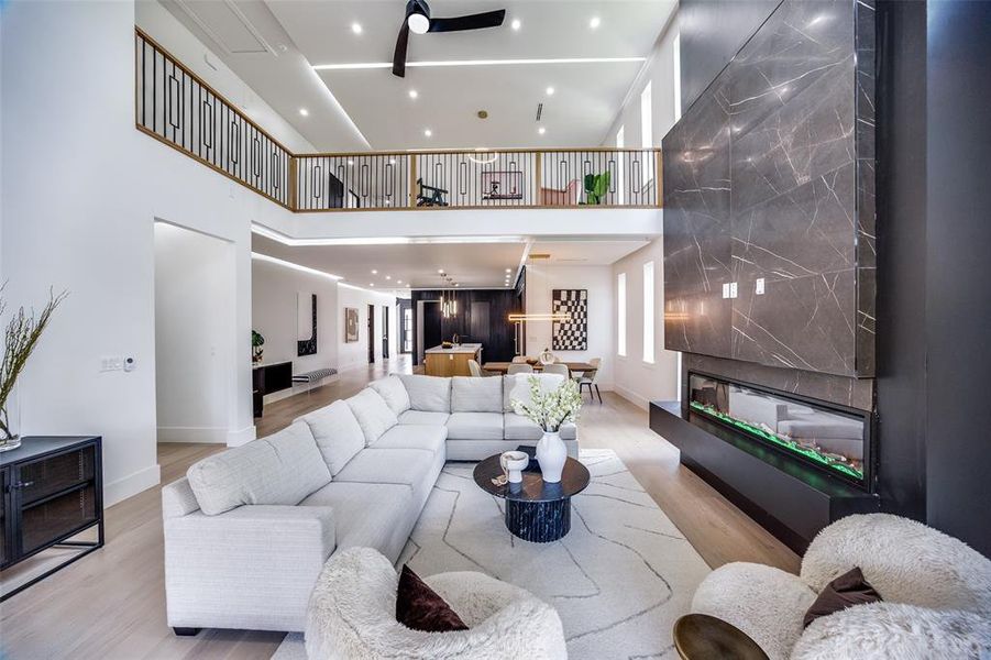 Living room featuring ceiling fan, a high ceiling, a large fireplace, and light hardwood / wood-style floors