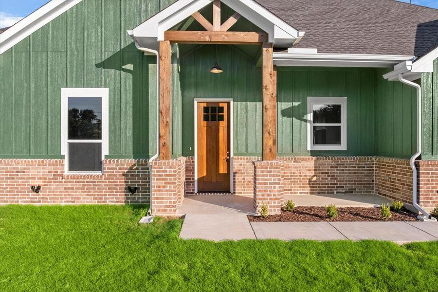 Doorway to property with a porch, board and batten siding, a lawn, and brick siding Doorway to property with a porch, board and batten siding, a lawn, and brick siding