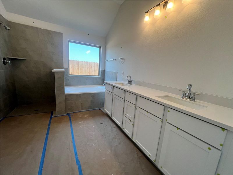 Full bath featuring double vanity, a bath, walk in shower, and vaulted ceiling