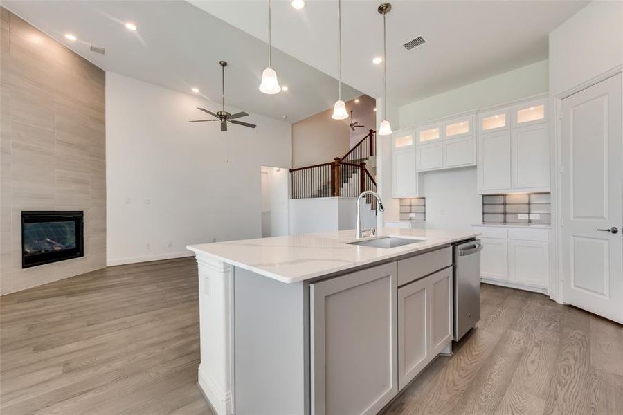 Kitchen featuring light hardwood / wood-style flooring, light stone countertops, a center island with sink, a tile fireplace, and sink