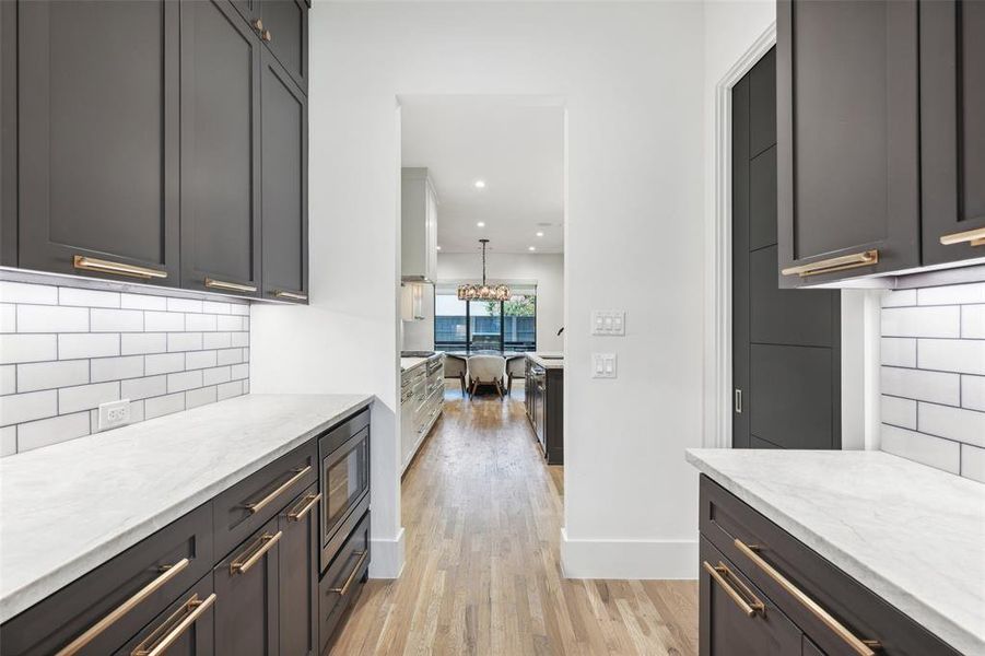 Kitchen with light hardwood / wood-style flooring, tasteful backsplash, hanging light fixtures, stainless steel microwave, and light stone countertops