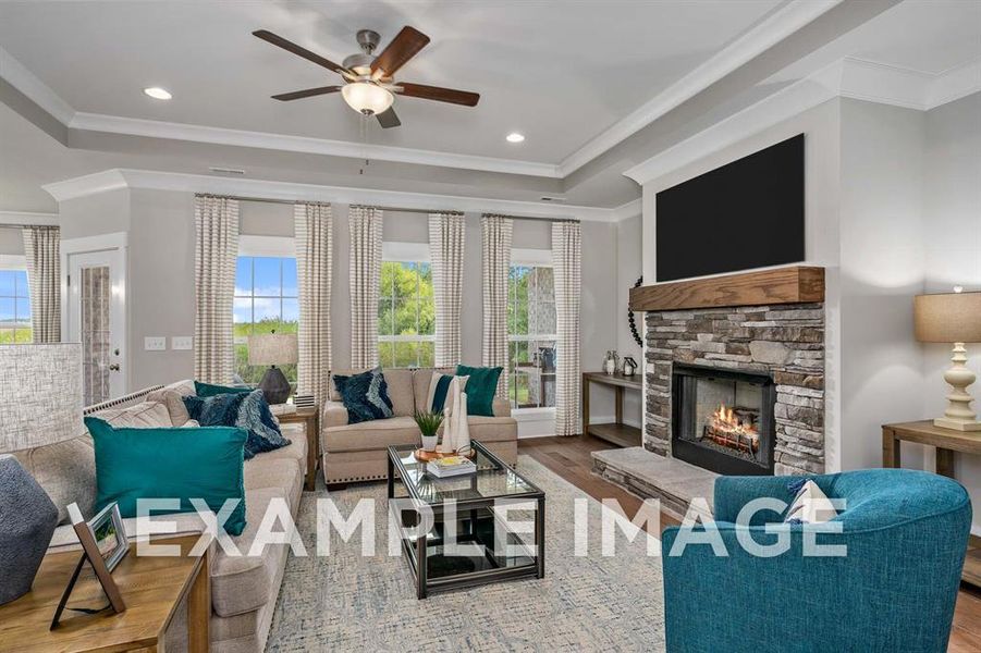 Living room with ceiling fan, a stone fireplace, crown molding, a tray ceiling, and hardwood / wood-style flooring