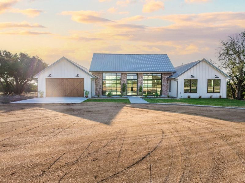 Modern farmhouse style home with board and batten siding, a garage, driveway, and a metal roof