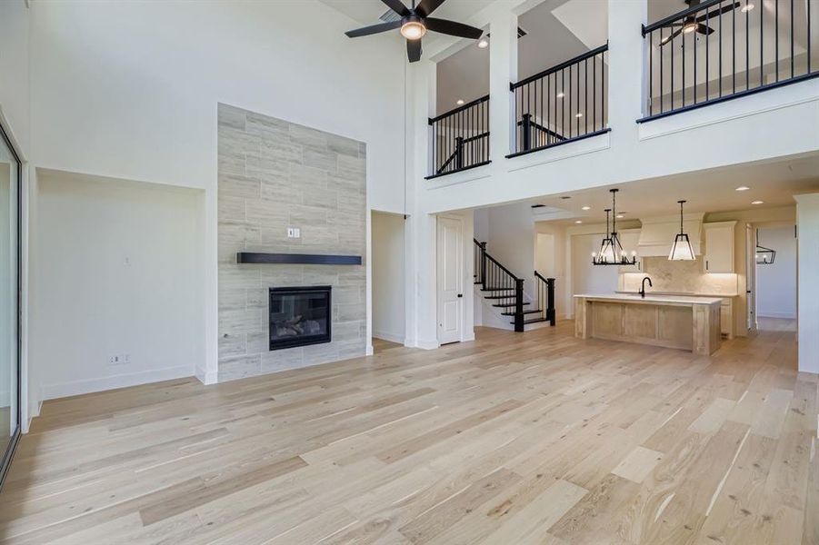 Unfurnished living room with light wood finished floors, a fireplace, a towering ceiling, ceiling fan, and stairway Unfurnished living room with light wood finished floors, a fireplace, a towering ceiling, ceiling fan, and stairway
