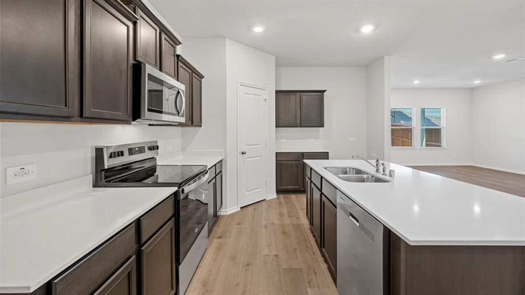 Kitchen with appliances with stainless steel finishes, light wood-style flooring, dark brown cabinetry, a center island with sink, and recessed lighting