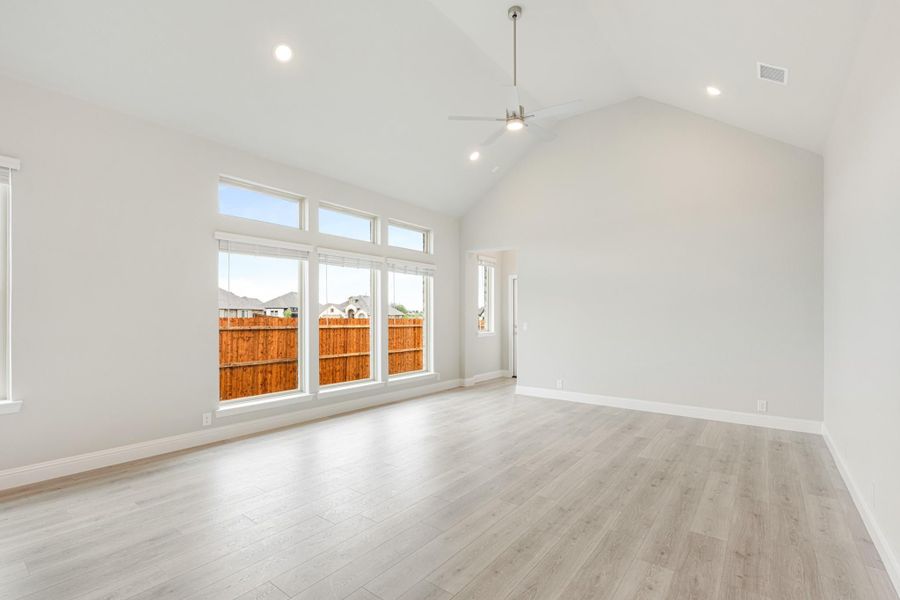 Empty living room with vaulted ceiling, ceiling fan, light wood floors, and large windows