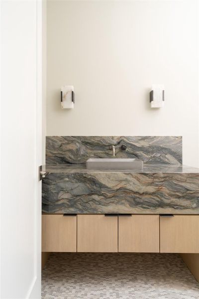 Downstairs powder room with a floating white oak rift-cut vanity topped in dramatic quartzite, complemented by sculptural Kelly Wearstler sconces and mosaic tile flrooring