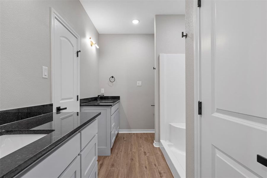 Bathroom with light wood-type flooring, two vanities, and a tub