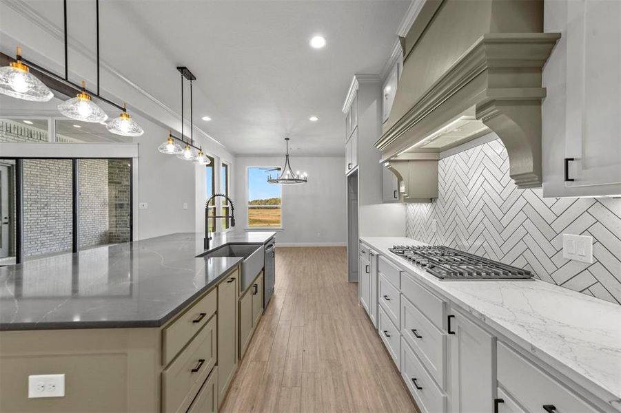 Kitchen featuring premium range hood, backsplash, pendant lighting, dark stone counters, and light wood-type flooring