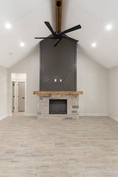 Unfurnished living room with a stone fireplace, recessed lighting, lofted ceiling, light wood-style flooring, and a ceiling fan
