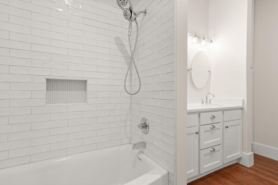 Modern white subway tile surround complements a sleek tub-shower combination and a vanity with a circular mirror. Modern white subway tile surround complements a sleek tub-shower combination and a vanity with a circular mirror.