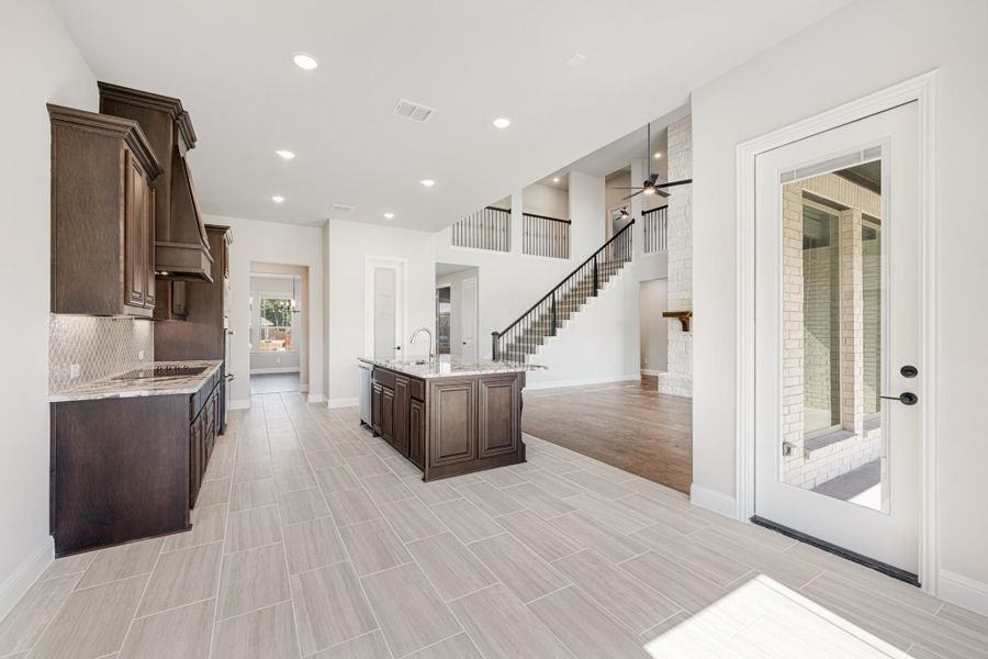 Open kitchen with dark wood cabinets, center island, tile floors, and staircase visible in background Open kitchen with dark wood cabinets, center island, tile floors, and staircase visible in background
