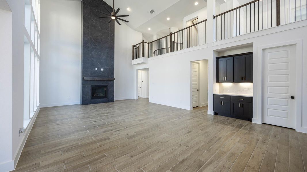 Unfurnished living room featuring a high ceiling, ceiling fan, a fireplace, light wood finished floors, and healthy amount of natural light