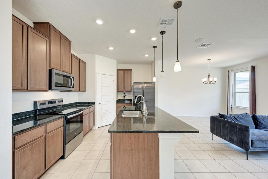A contemporary kitchen features an island with seating, dark granite counters, and stainless appliances.