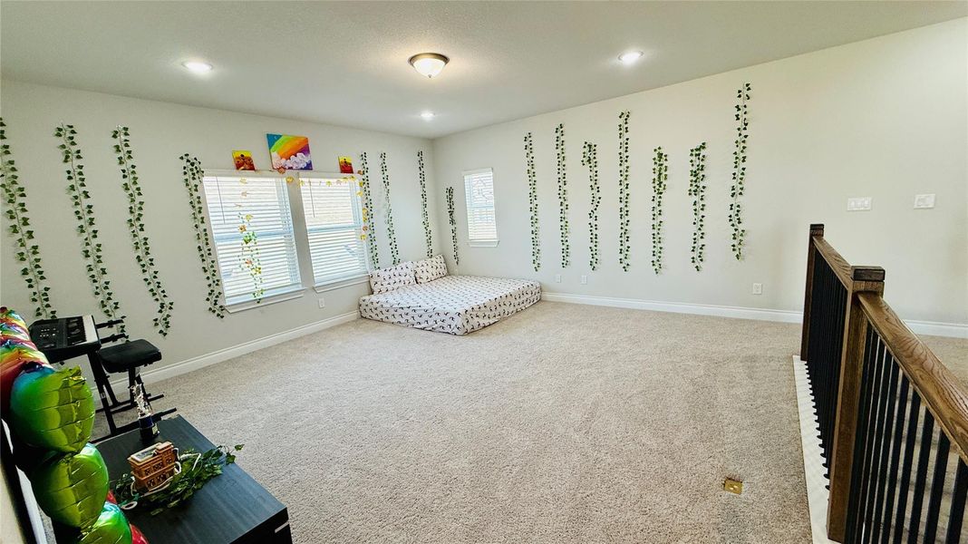 A spacious room features plush carpeting and abundant natural light from multiple windows.