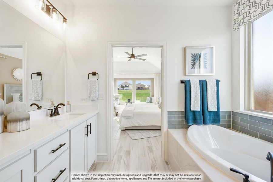 Ensuite bathroom with white vanity, soaking tub, and open view into bedroom with ceiling fan Ensuite bathroom with white vanity, soaking tub, and open view into bedroom with ceiling fan