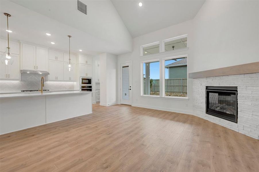 The open concept living area features light-toned flooring, a fireplace with a stone surround, and large windows