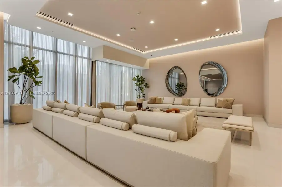 Floor-to-ceiling windows with floor-length drapery, recessed tray ceiling with integrated cove lighting, recessed ceiling lights, and polished stone flooring