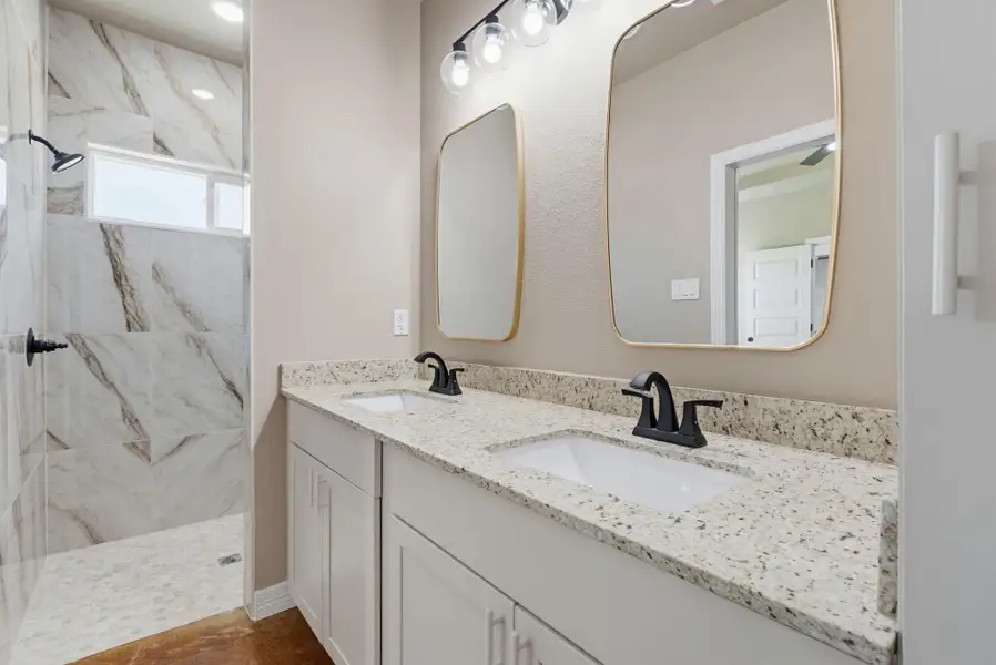 Full bath featuring a marble finish shower and double vanity